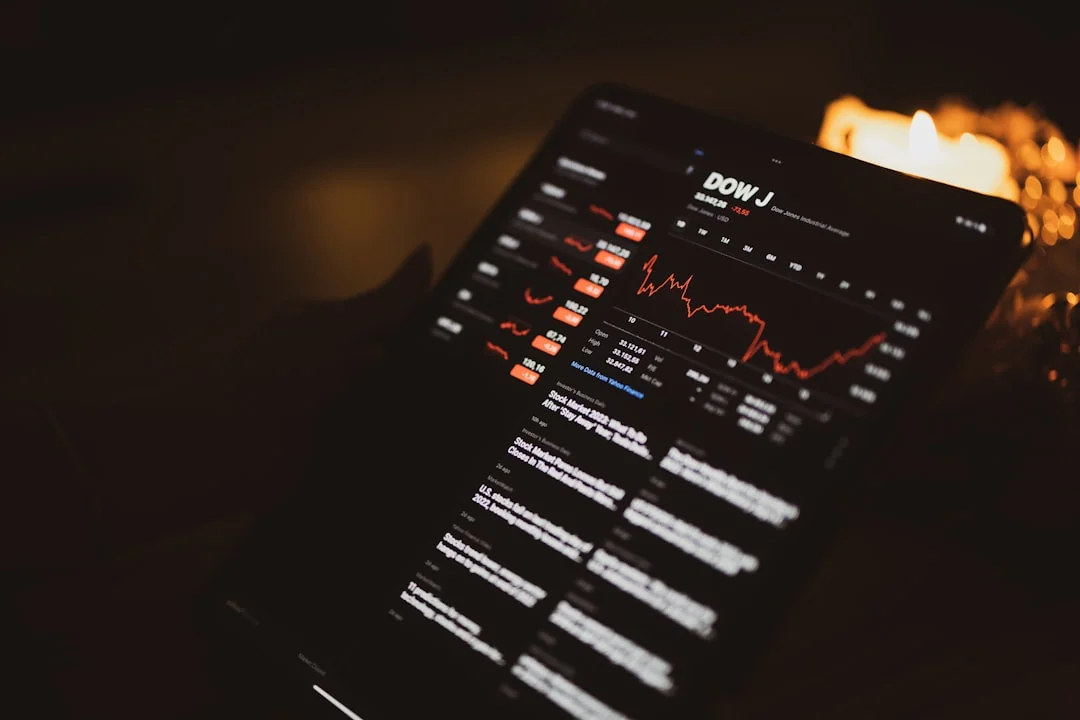 Person analyzes stock data with a smartphone and laptop, indoors.